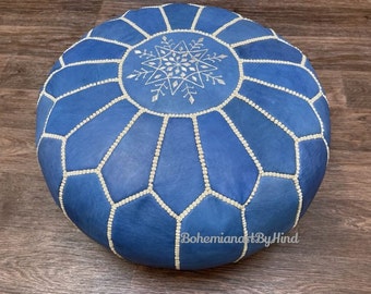 May include: Blue leather pouf with white stitching and a white snowflake design. The pouf is round and has a tufted surface.