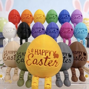 May include: A selection of colourful Easter egg figurines with articulated legs. Each egg is a different colour and features the words "Happy Easter" and a bunny silhouette. The eggs are arranged on a clear display shelf.