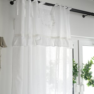 Può includere: Tende bianche in voile con un bordo a balze e un monogramma ricamato "PM" con un fiocco e una corona di alloro.