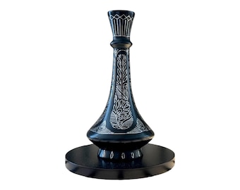May include: A black decorative vase with a slender neck and a wide base, featuring intricate white etched floral and leaf patterns. The vase stands on a circular black pedestal base, showcasing a smooth finish and detailed line work throughout.