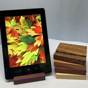 May include: A black tablet with a colorful image of autumn leaves is propped up on a wooden stand. The stand is made of multiple layers of wood, each a different shade of brown.