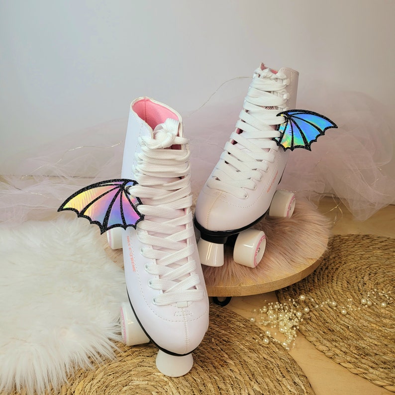 May include: White roller skates with pink accents and iridescent wings attached to the laces. The skates have white wheels and a white base.