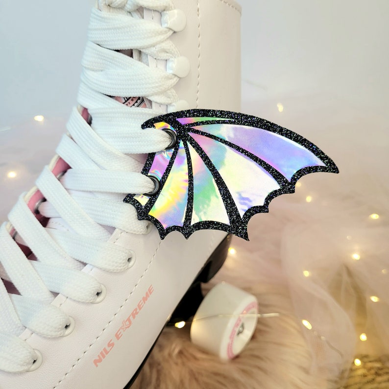 May include: White roller skates with pink laces and a holographic iridescent dragon wing charm attached to the laces. The skates have the text "NILS EXTREME" printed on the side.