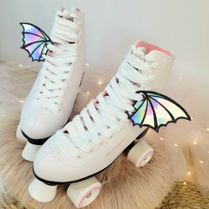 May include: A pair of white roller skates with iridescent wings attached to the laces. The skates have pink accents and the words "NILS EXTREME" are printed on the side.