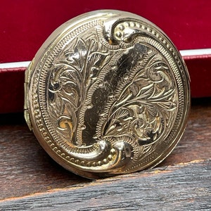 May include: A gold oval locket with an intricate floral design engraved on the front.