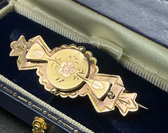 May include: A gold and rose gold brooch with a floral design in the center. The brooch is in a blue velvet box.