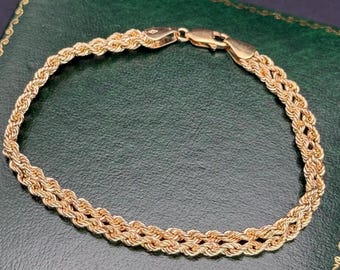 以下が含まれることがあります： 二重のロープチェーンデザインが特徴のローズゴールドブレスレット。このジュエリーは、2本のねじれた金属リンクが絡み合って連続した円形を形成しており、磨き上げられたロブスタークラスプで留められています。