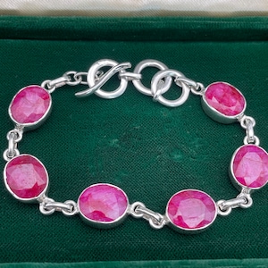 Può includere: Un braccialetto d'argento con chiusura a scorrimento e pietre preziose di rubino di forma ovale.