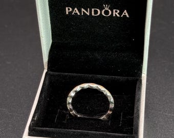 May include: A silver ring with a geometric design is displayed inside a white Pandora box with the brand name printed on the lid. The ring has a series of triangular facets around its band. The box has a black velvet interior.