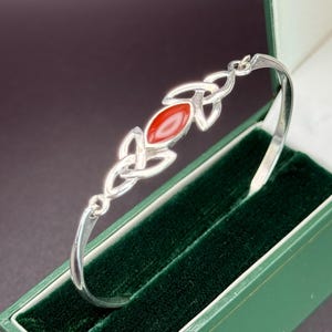 May include: A silver bangle bracelet with a Celtic knot design and a red carnelian stone.