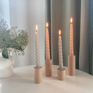 May include: Four candlesticks with four twisted candles, two are a light beige color and two are a light peach color. The candlesticks are made of wood and have a natural finish. The candles are lit and the flames are visible.