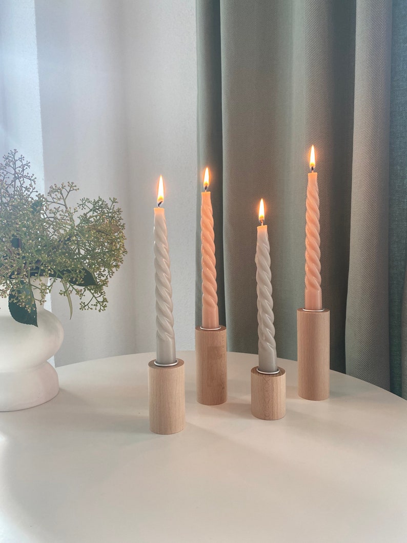 May include: Four candlesticks with four twisted candles, two are a light beige color and two are a light peach color. The candlesticks are made of wood and have a natural finish. The candles are lit and the flames are visible.