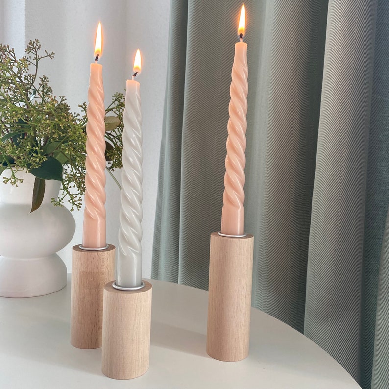 May include: Three twisted candles in wooden holders. The candles are lit and are a light pink and white color.
