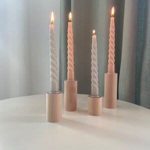 May include: Four candles in wooden holders. Two candles are a light pink color and two are a light gray color. The candles are all twisted and have a flame on top.