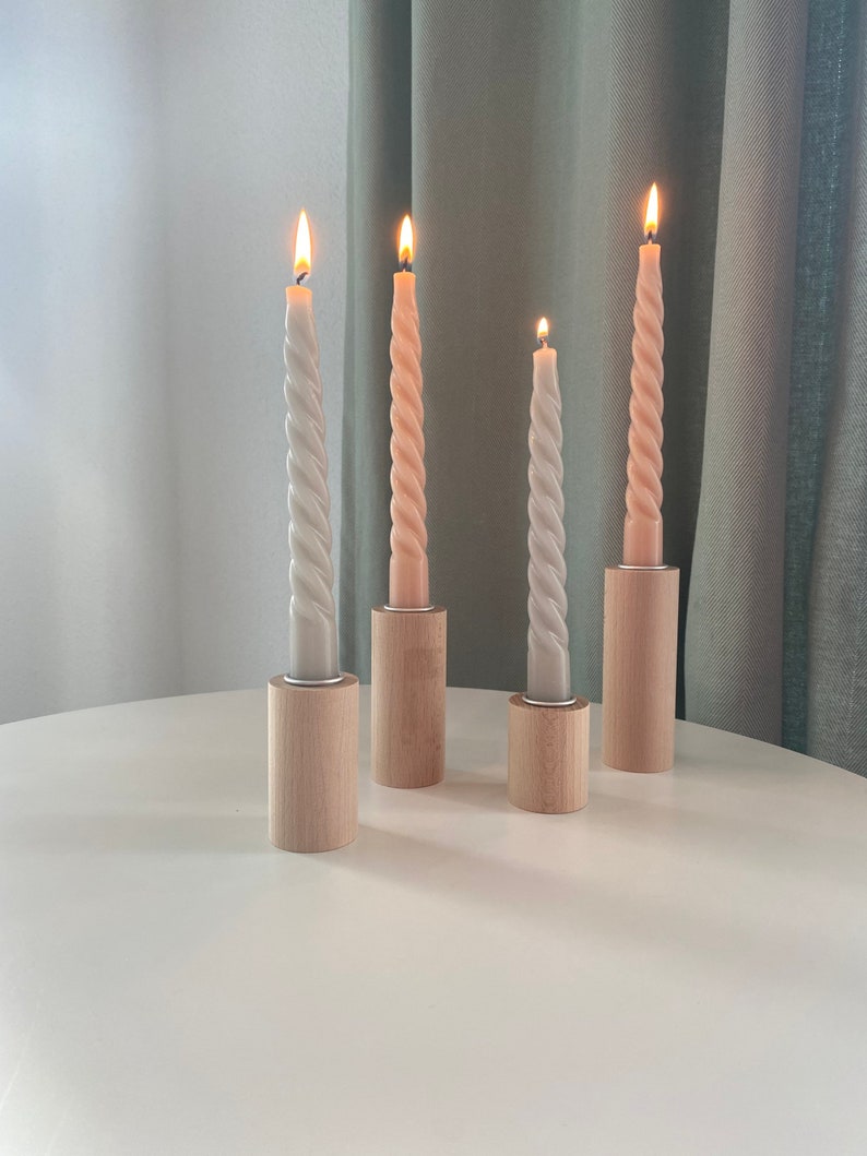 May include: Four candles in wooden holders. Two candles are a light pink color and two are a light gray color. The candles are all twisted and have a flame on top.