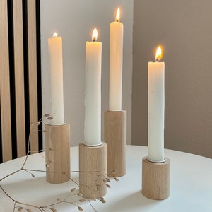 May include: Four white candles burning in wooden candle holders on a white table. The candle holders are made of natural wood and have a simple design.
