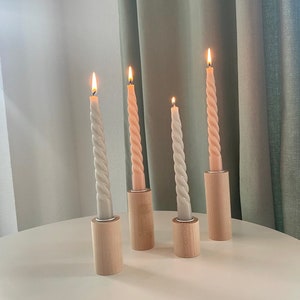 May include: Four candlesticks with twisted candles, two are light gray and two are light pink, all are lit and sitting on a white table.