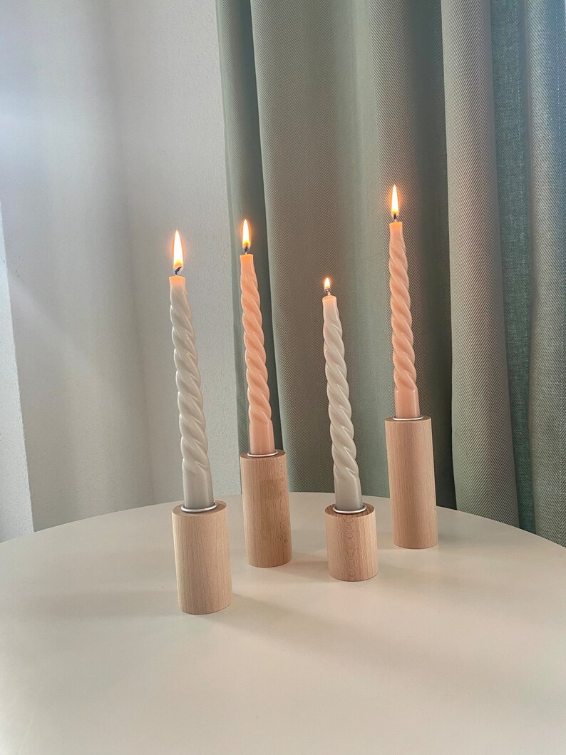 May include: Four candlesticks with twisted candles, two are light gray and two are light pink, all are lit and sitting on a white table.