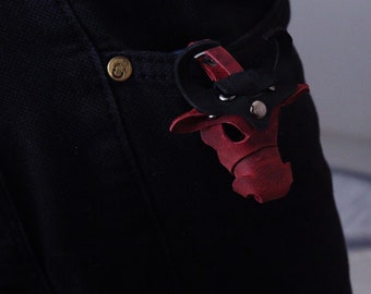 May include: A red leather bull keychain with black accents hanging from a black belt loop.