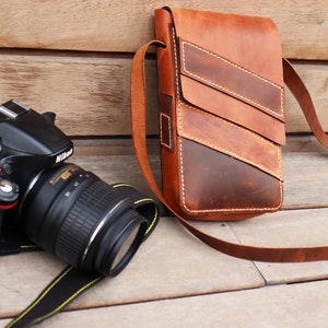 May include: A black DSLR camera with a lens attached, and a brown leather camera bag with a strap.