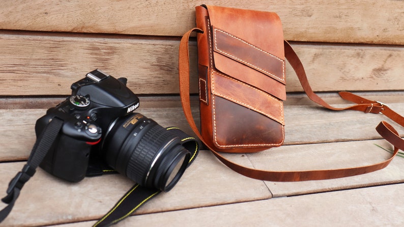 May include: A black DSLR camera with a lens attached, and a brown leather camera bag with a strap.