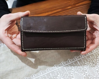 May include: A brown leather wallet with white stitching. The wallet is closed and has a flap.