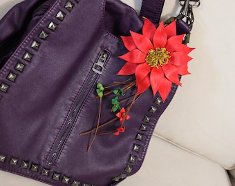 Könnte beinhalten: Eine lila Lederhandtasche mit silbernen Nieten und einer roten Blumenverzierung.