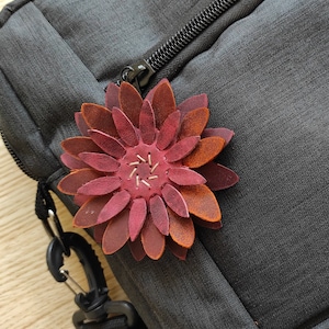 May include: A burgundy leather flower with a stitched center, attached to a black bag.
