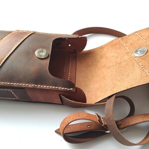 May include: A brown leather crossbody bag with a flap closure and a magnetic snap. The bag has a single strap and a small pocket on the front.