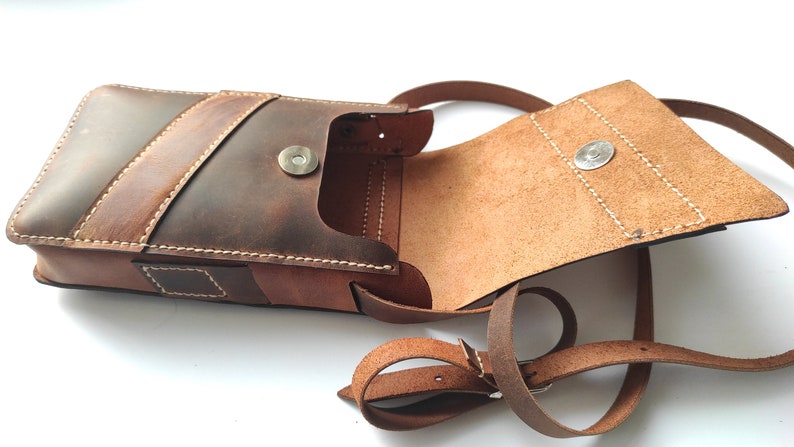 May include: A brown leather crossbody bag with a flap closure and a magnetic snap. The bag has a single strap and a small pocket on the front.