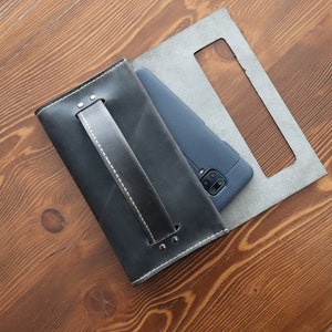 May include: A black leather phone case with a stitched handle and a gray leather backing. The case is open and a blue smartphone is inside.