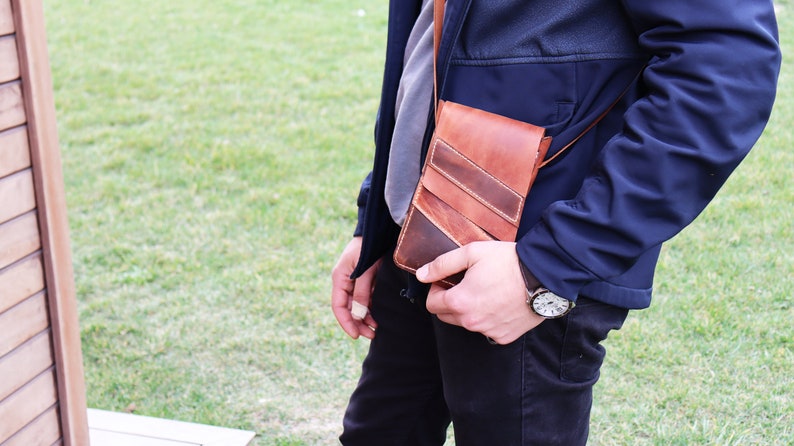 May include: A brown leather crossbody bag with a strap. The bag has a flap closure and a stitched design.