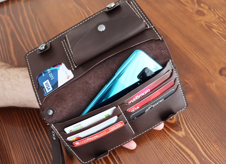 May include: A brown leather wallet with multiple card slots and a phone pocket. The wallet is open and has several cards and a turquoise phone inside.