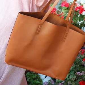 Könnte beinhalten: Eine braune Ledertasche mit zwei Henkeln. Die Tasche ist groß und geräumig und eignet sich perfekt für den Transport von Alltagsgegenständen.