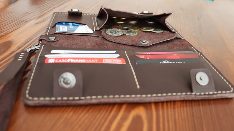 May include: A brown leather wallet with a zipper closure, multiple card slots, and a coin pocket. The wallet is open and shows several cards and coins inside.