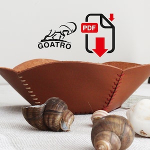 May include: A brown leather bowl with red stitching. The bowl is sitting on a white tablecloth with seashells and snails around it. The image also includes a logo for "GOATRO" and a PDF download icon.
