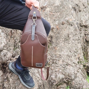 Puede incluir: Un bolso de cuero marr&oacute;n cruzado con cierre de solapa y correa. El bolso tiene un dise&ntilde;o cosido y un peque&ntilde;o bolsillo en la parte delantera.