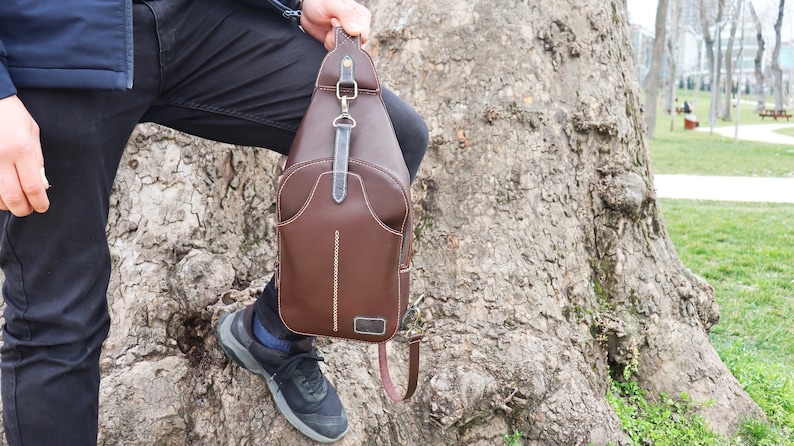 Puede incluir: Un bolso de cuero marr&oacute;n cruzado con cierre de solapa y correa. El bolso tiene un dise&ntilde;o cosido y un peque&ntilde;o bolsillo en la parte delantera.