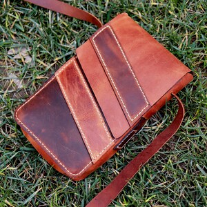 May include: A brown leather crossbody bag with a flap closure and a long strap. The bag has a distressed look and is made of multiple pieces of leather sewn together.