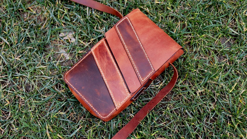 May include: A brown leather crossbody bag with a flap closure and a long strap. The bag has a distressed look and is made of multiple pieces of leather sewn together.