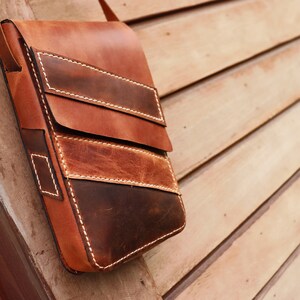 May include: A brown leather crossbody bag with a flap closure and multiple pockets. The bag has a distressed look and is made of high-quality leather.