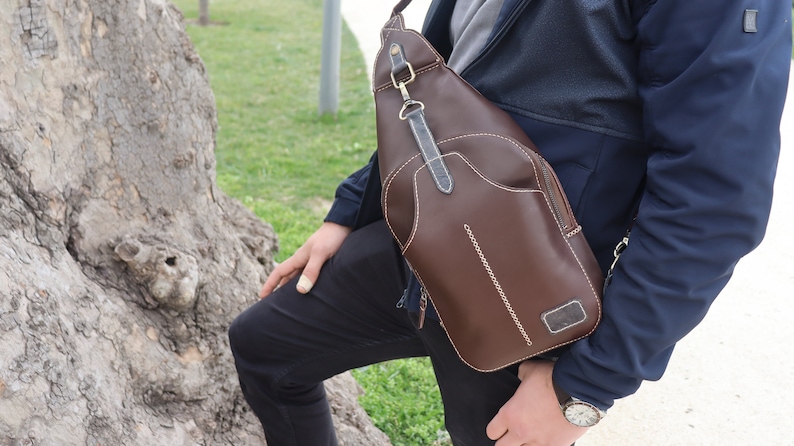 Puede incluir: Un bolso bandolera de cuero marr&oacute;n con cierre de solapa y un bolsillo con cremallera. El bolso tiene una correa ajustable para un ajuste c&oacute;modo en el cuerpo.