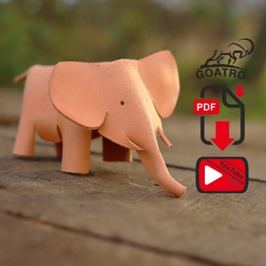 Peut inclure: Une figurine d'éléphant en cuir rose clair. La figurine est posée sur une surface en bois. L'image comprend également un logo pour Goatro, une icône de téléchargement PDF et une icône de vidéo YouTube.