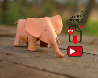 Könnte beinhalten: Eine hellrosa Leder-Elefantenfigur. Die Figur steht auf einer Holzoberfläche. Das Bild enthält auch ein Logo für Goatro, ein PDF-Download-Symbol und ein YouTube-Video-Symbol.