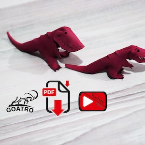 May include: Two red papercraft dinosaurs on a woodgrain surface. A PDF download icon and a YouTube video icon are below the dinosaurs. The text "GOATRO" is below the PDF icon.