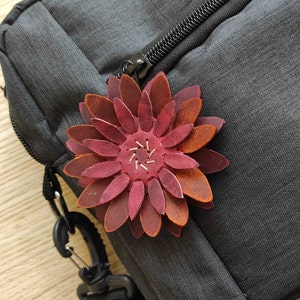 May include: A dark grey backpack with a zip fastening and a red leather flower embellishment.