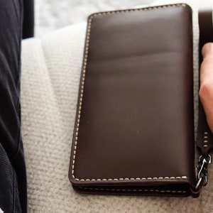 May include: A brown leather wallet with a chain attached to the side. The wallet is closed and has white stitching around the edges.