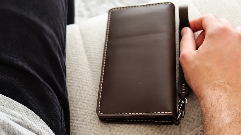 May include: A brown leather wallet with a chain attached to the side. The wallet is closed and has white stitching around the edges.