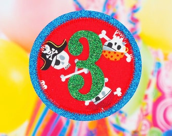 May include: A blue and red felt applique with a green glitter number three and a pirate design. The applique is perfect for a birthday party or craft project.