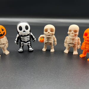 Könnte beinhalten: Fünf Halloween-Figuren. Zwei sind orangefarbene Kürbiskopf-Skelette, eines mit einem grünen Stiel. Zwei sind beige Skelette, und eines ist ein schwarz-weißes Skelett. Alle stehen aufrecht.